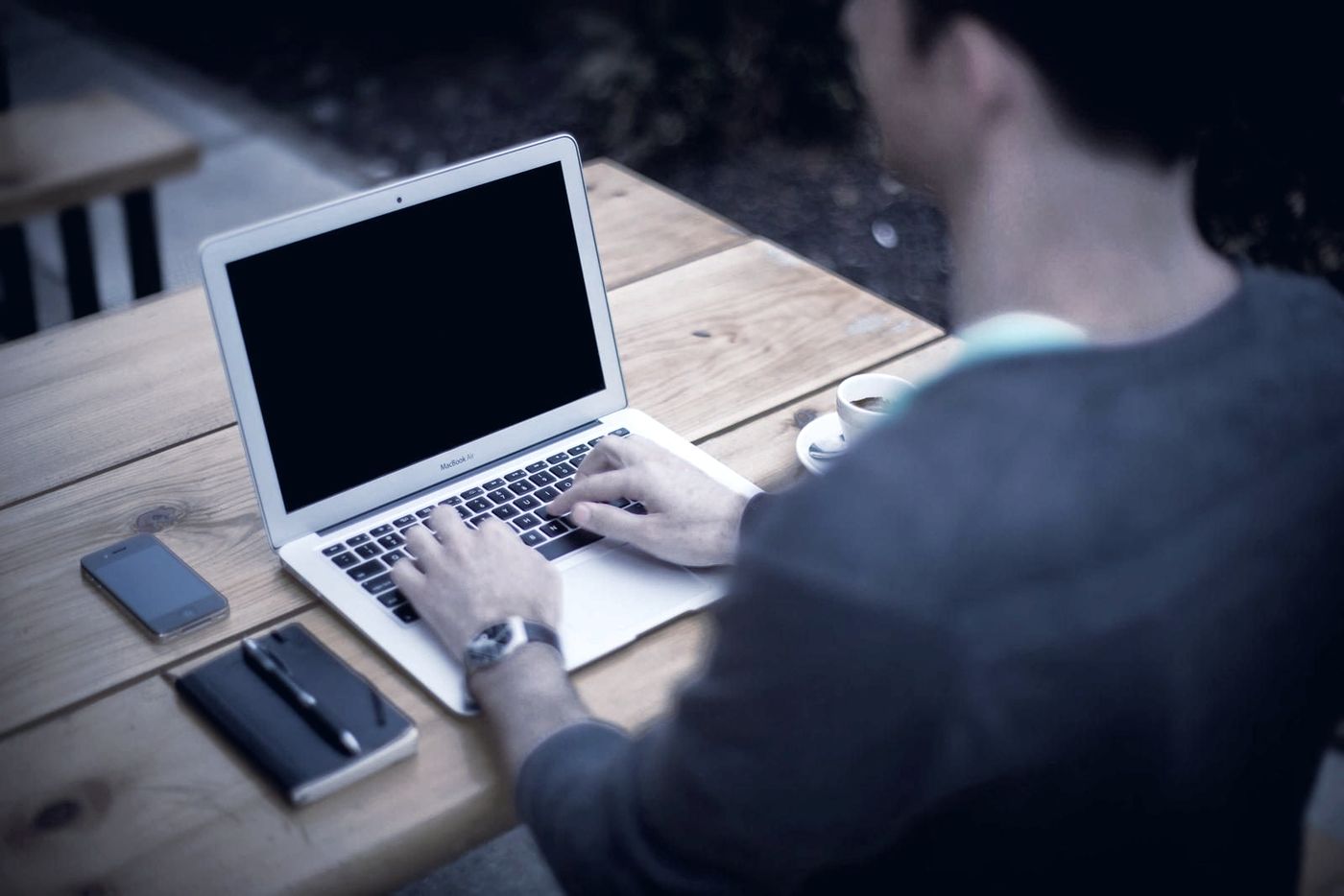A person typing on a laptop at a wooden table.