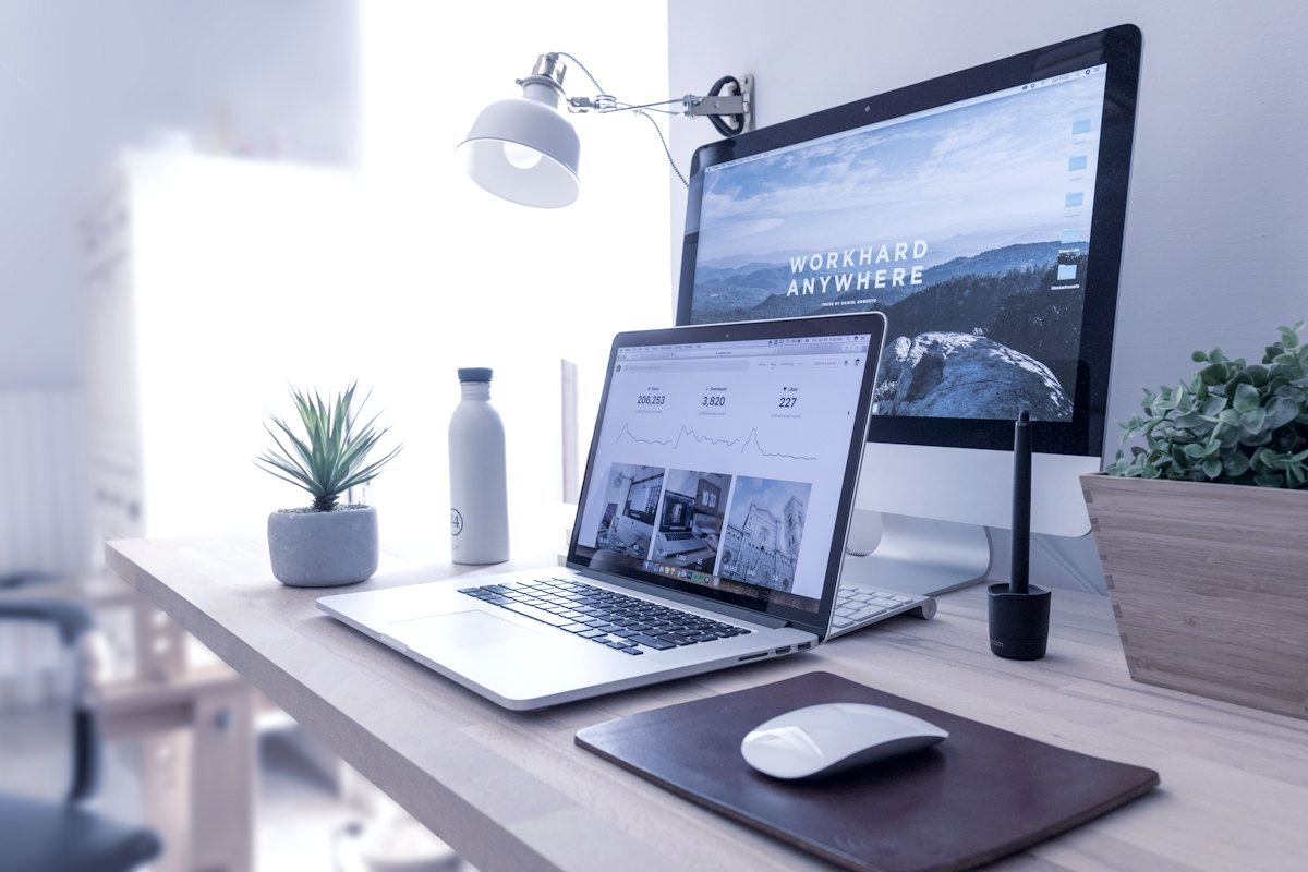 A laptop and desktop monitor showing a web application on a bright desk.